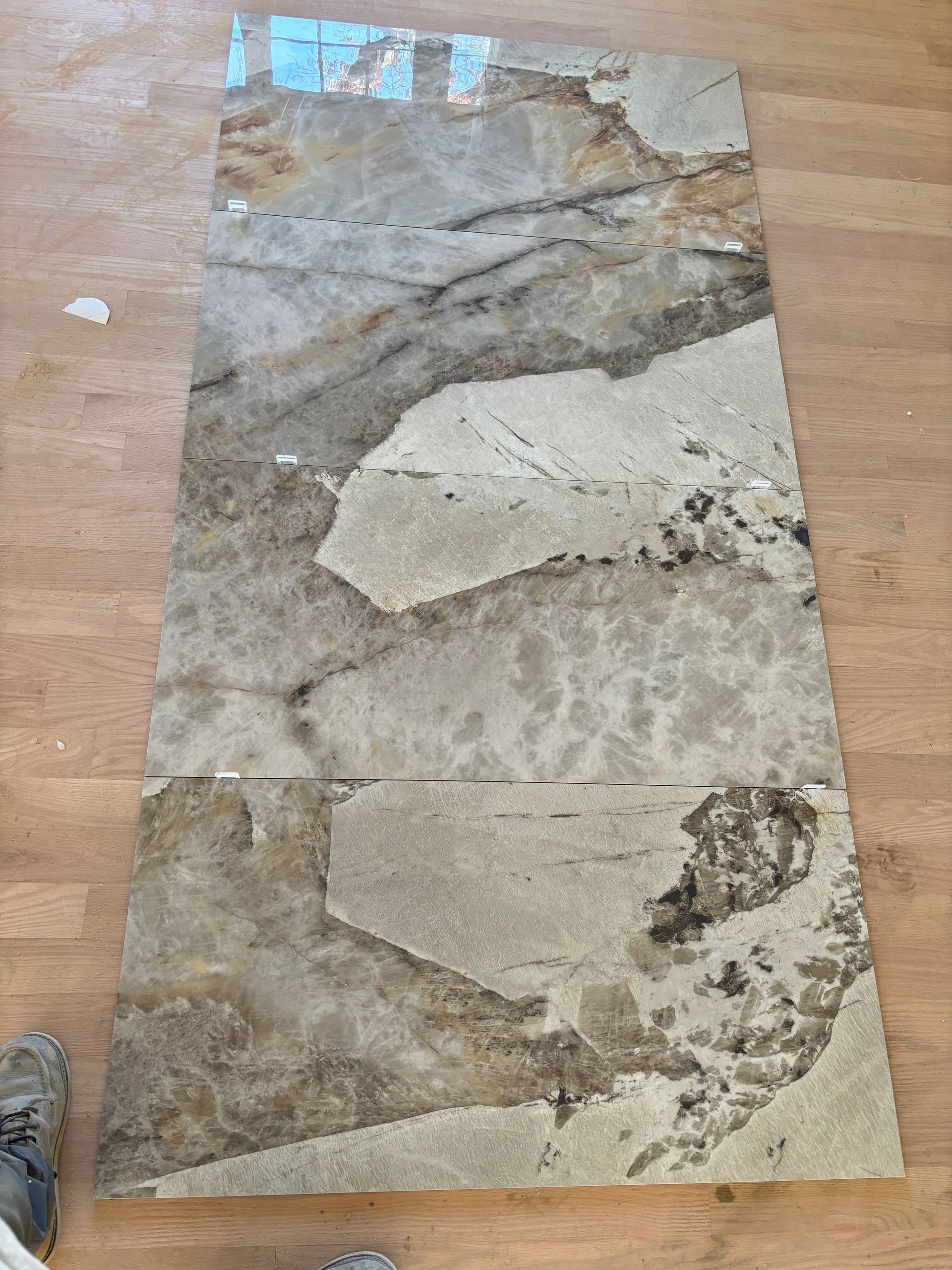 Granite countertop slab with tan, gray, and brown veining, lying on a wooden floor.