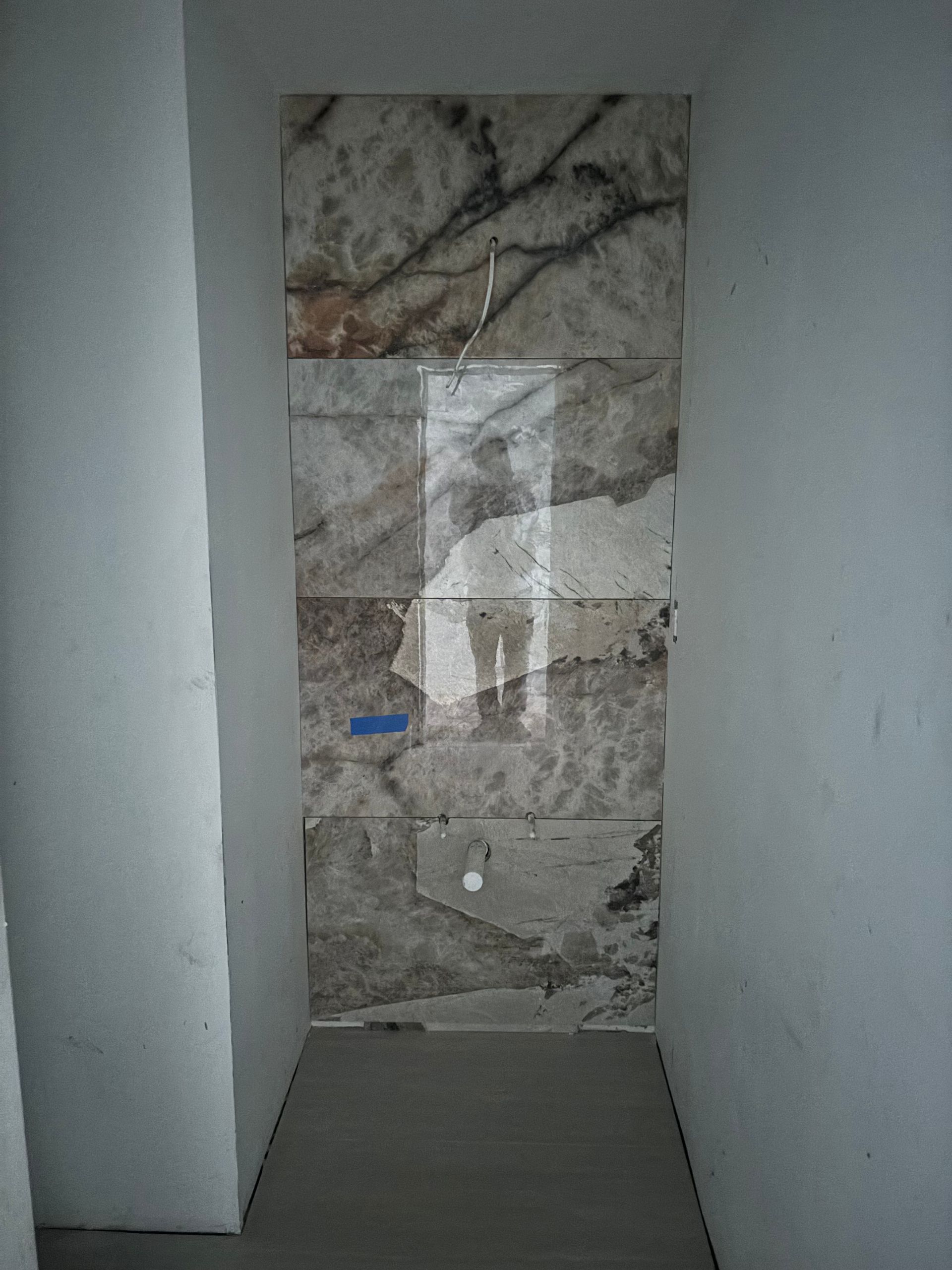 Narrow alcove with light marble tiles on the back wall, unfinished construction.