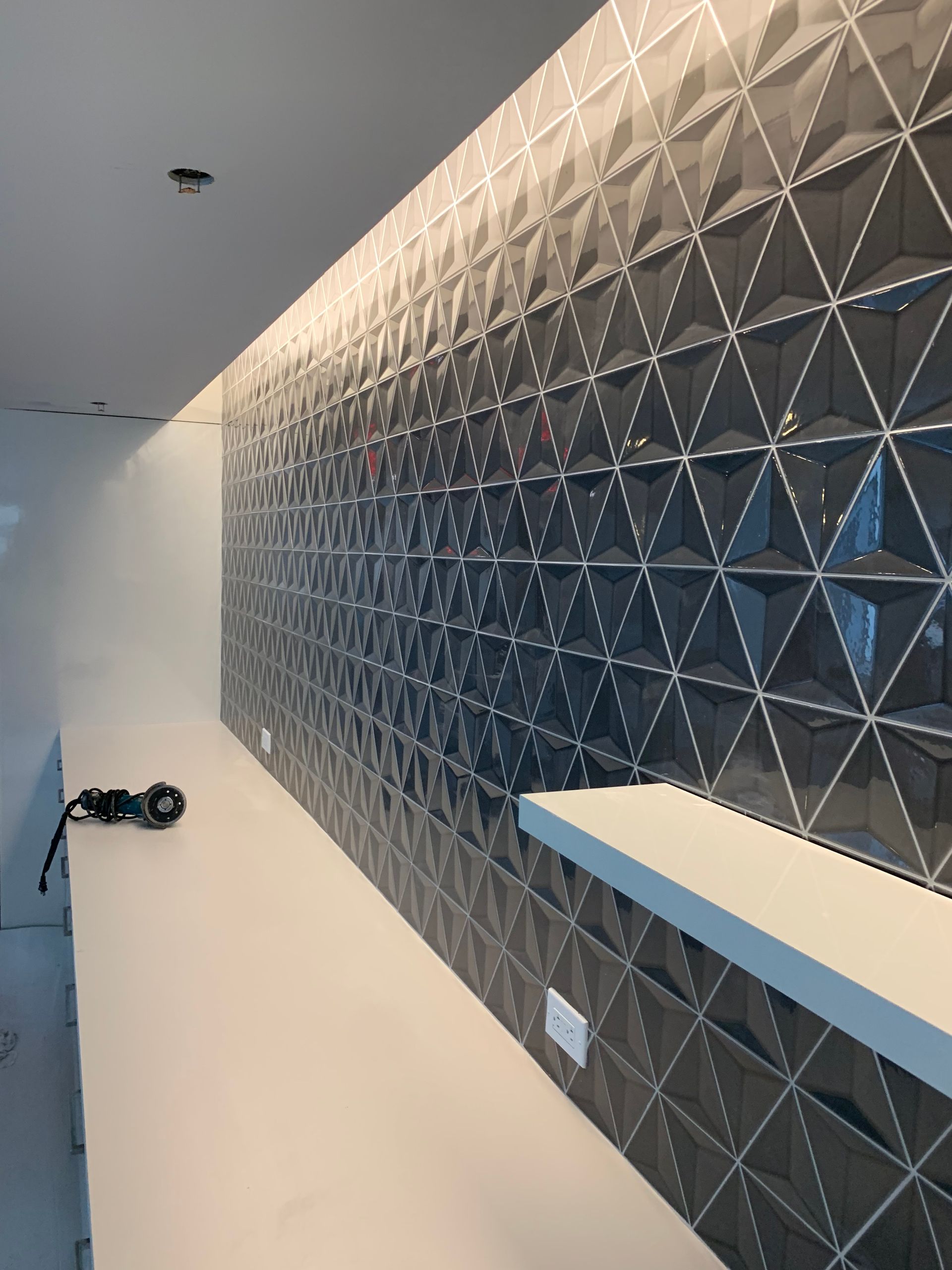 Dark grey textured tile wall with white counter, recessed lighting.