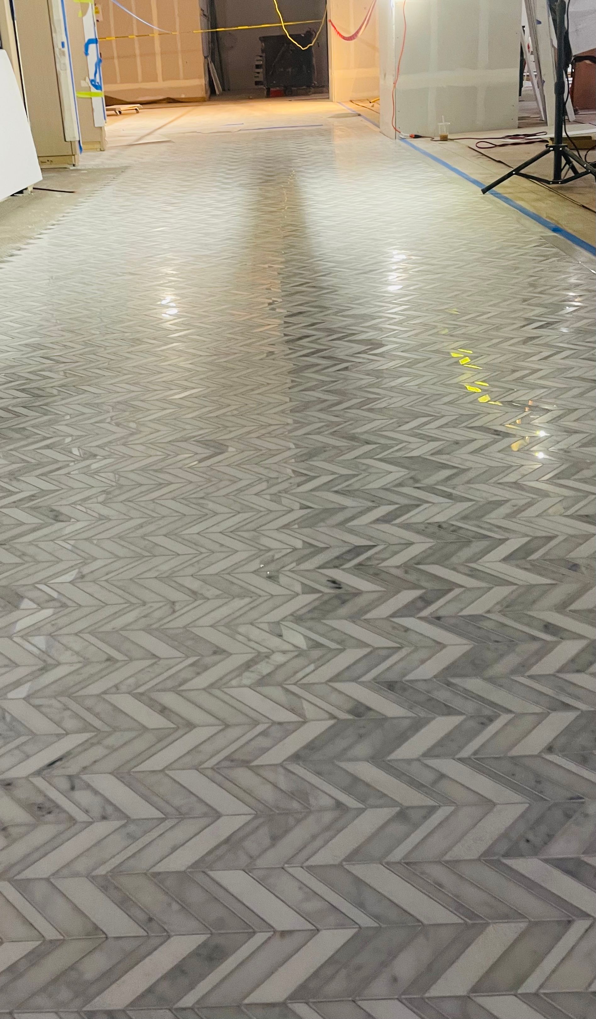 Herringbone-patterned marble floor in a hallway under construction, reflecting overhead lights.