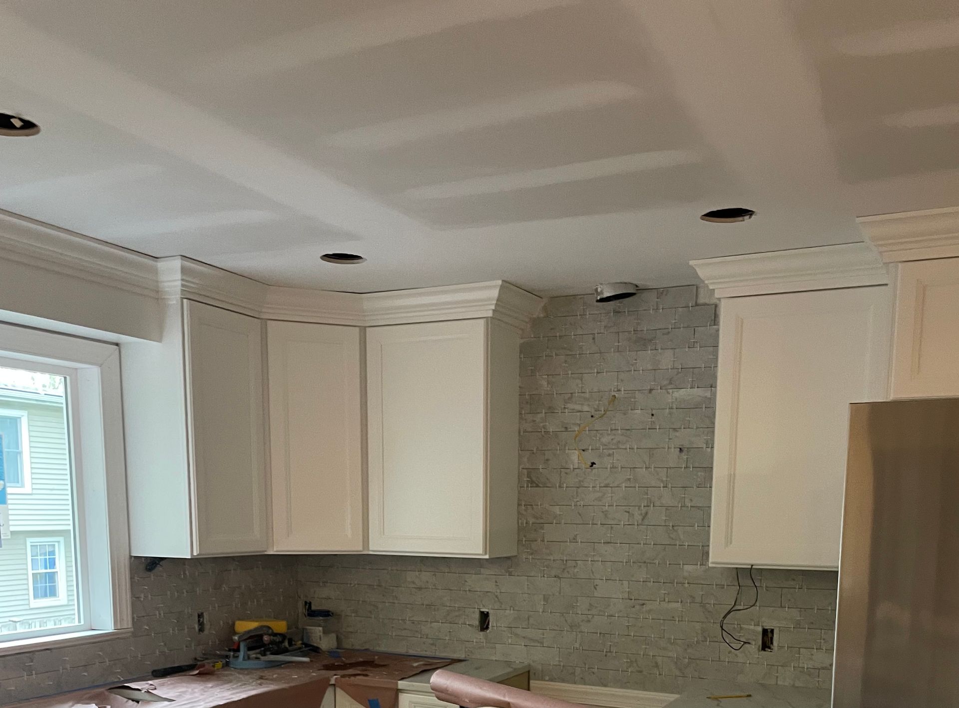 Kitchen under construction: white cabinets, brick backsplash, recessed lighting, and crown molding.