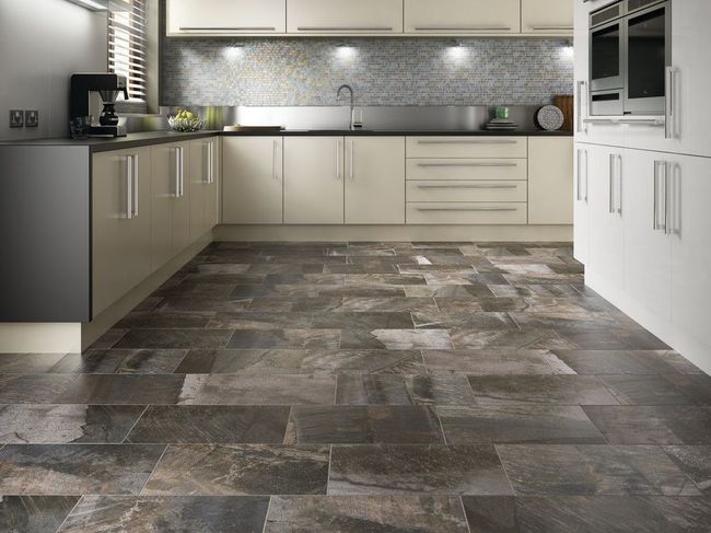 Kitchen with dark stone-like tiled floor, cream cabinets, stainless steel sink, and a coffee maker.