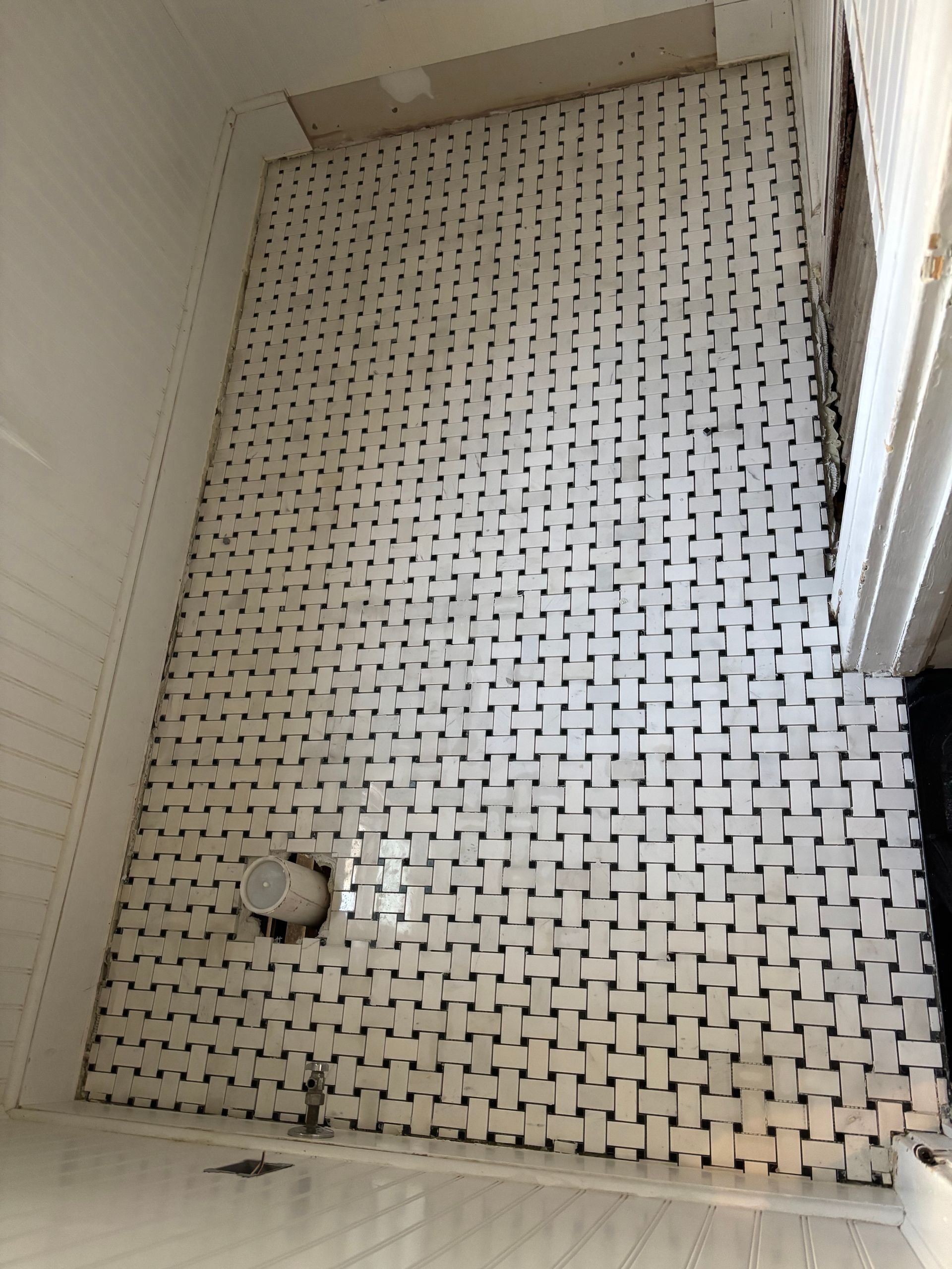 Bathroom floor tiled with a black and white geometric pattern, viewed from above.