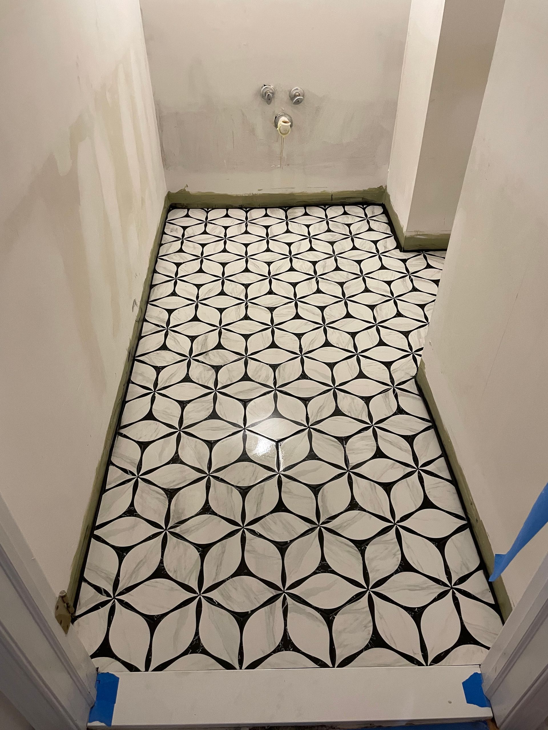 Bathroom with patterned black and white floor tiles. Walls are white and unfinished.