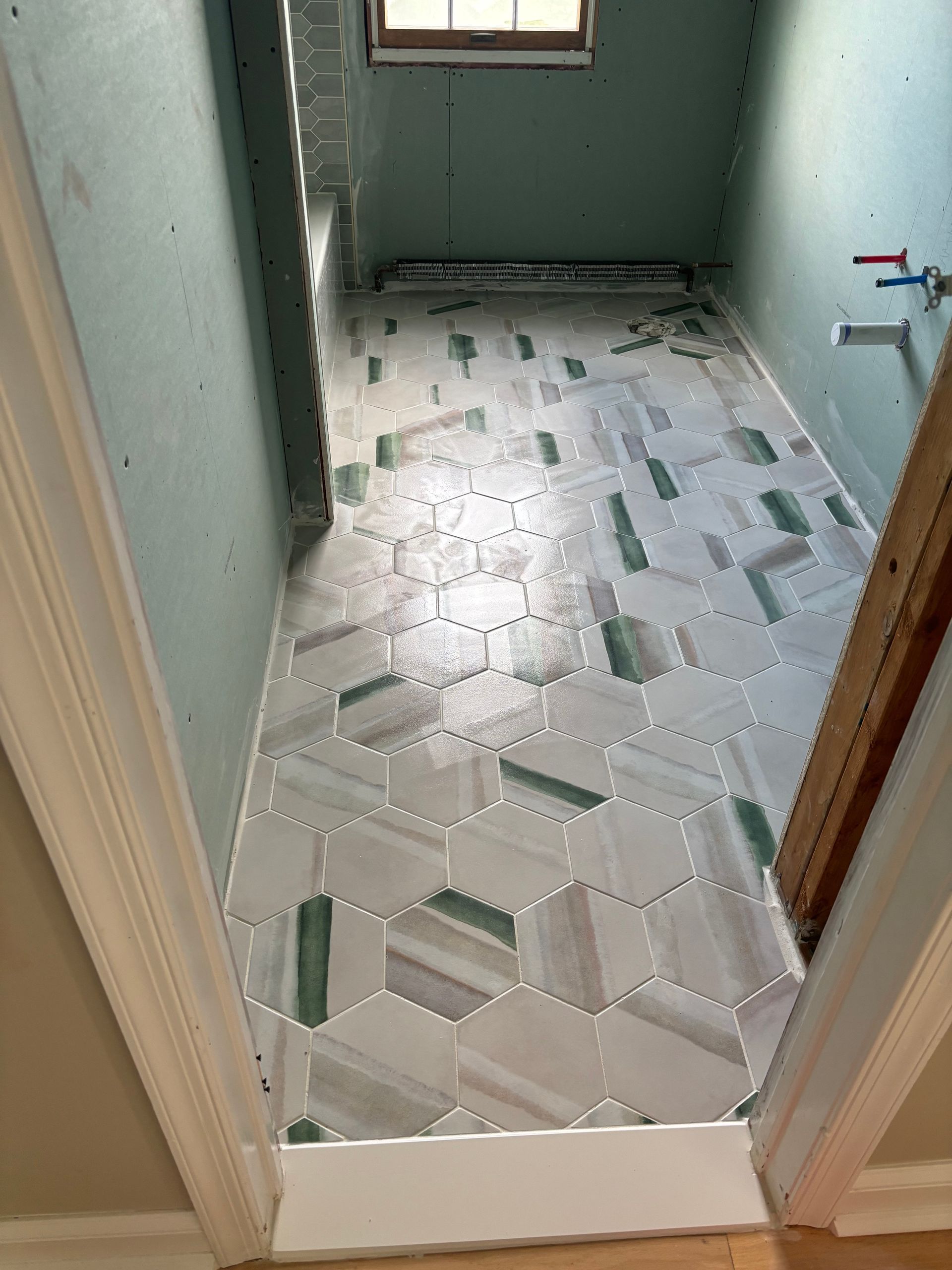 Bathroom floor in progress; white, gray and green hexagonal tiles being installed.