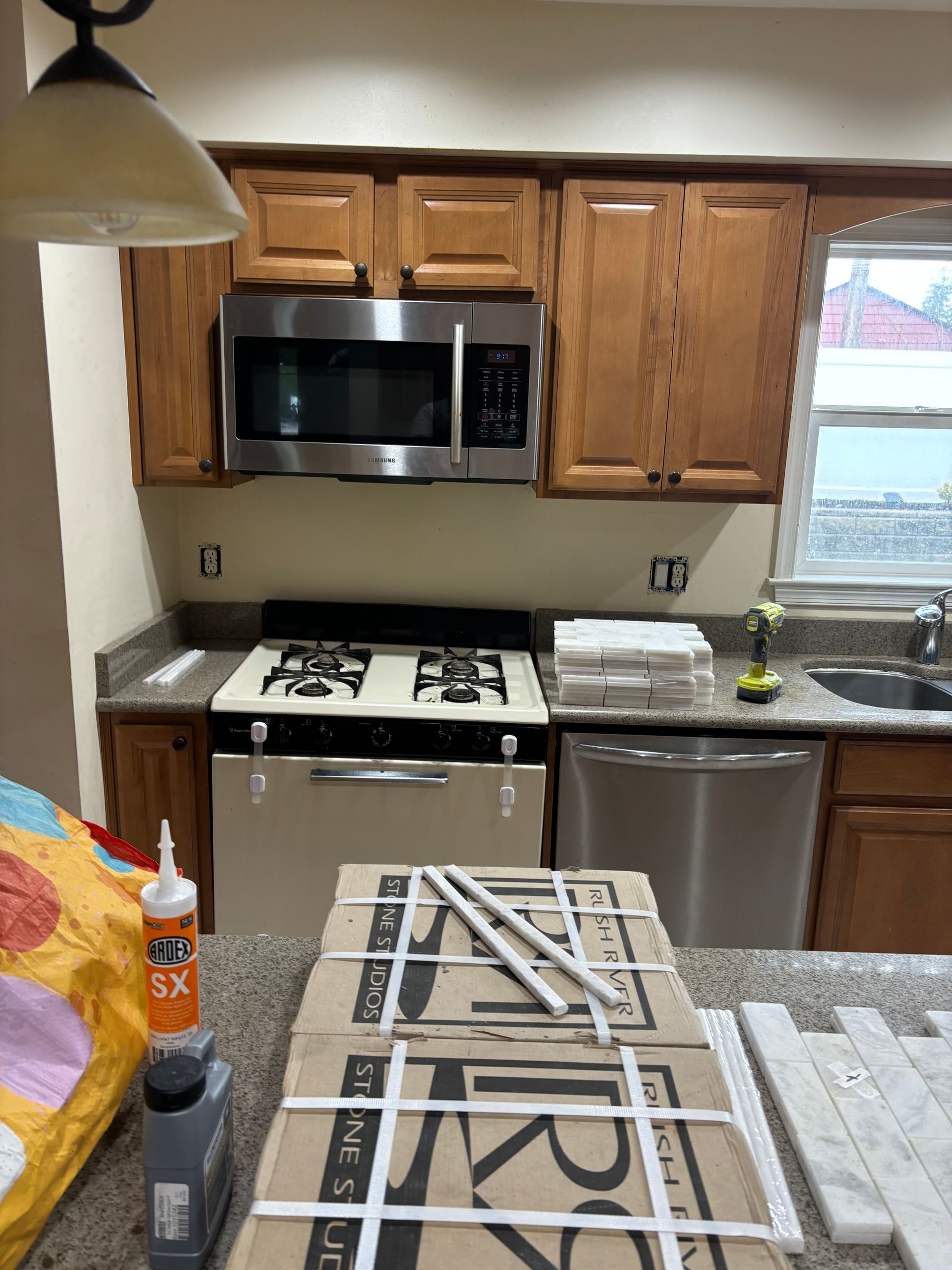 Kitchen with cabinets, stove, microwave, and dishwasher. Boxes of tile sit on the counter.