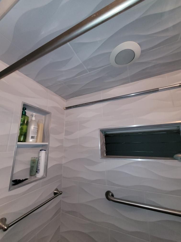 Bathroom with gray wavy tile, recessed shelf with toiletries, grab bars, and a light.