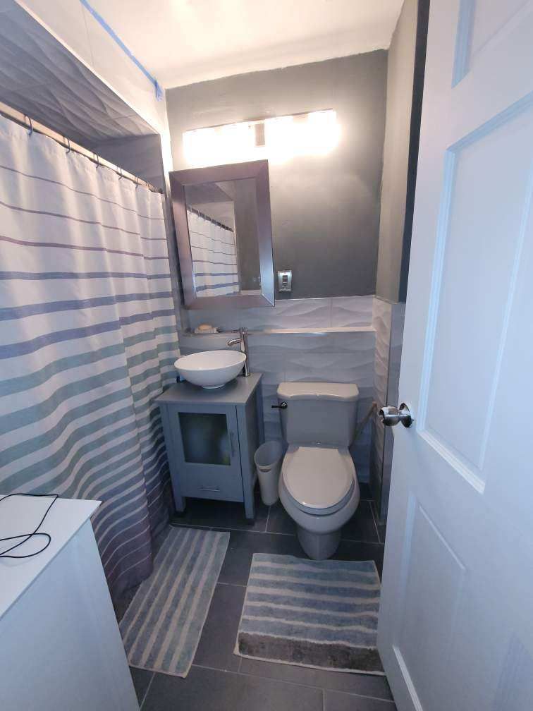 Small bathroom with toilet, sink, mirror, shower curtain, and door; grey, white, and blue colors.