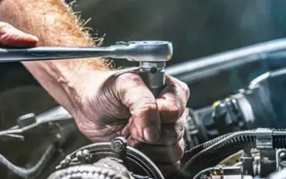 Hand gripping a wrench to tighten an engine bolt in a car repair setting