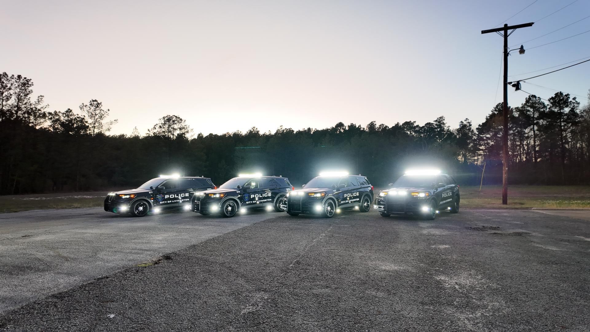 Four black SUVs with bright roof lights parked on a gravel lot at dusk.