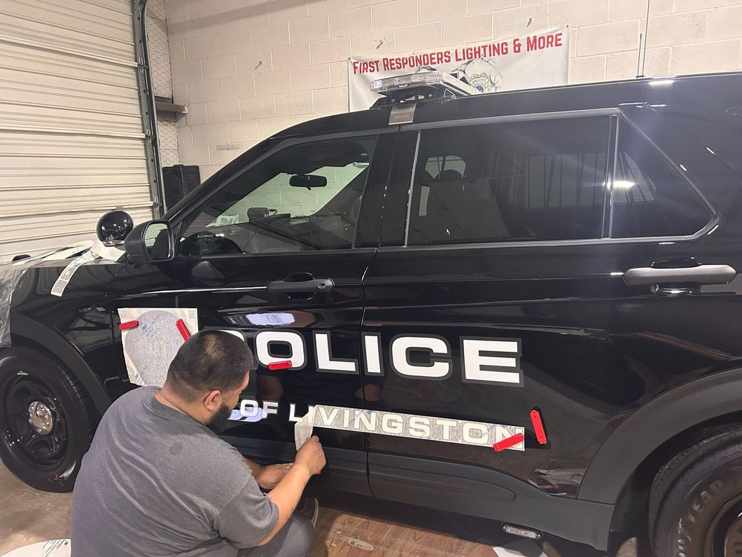 A person applying decals to a black police SUV. The vehicle is in a garage.