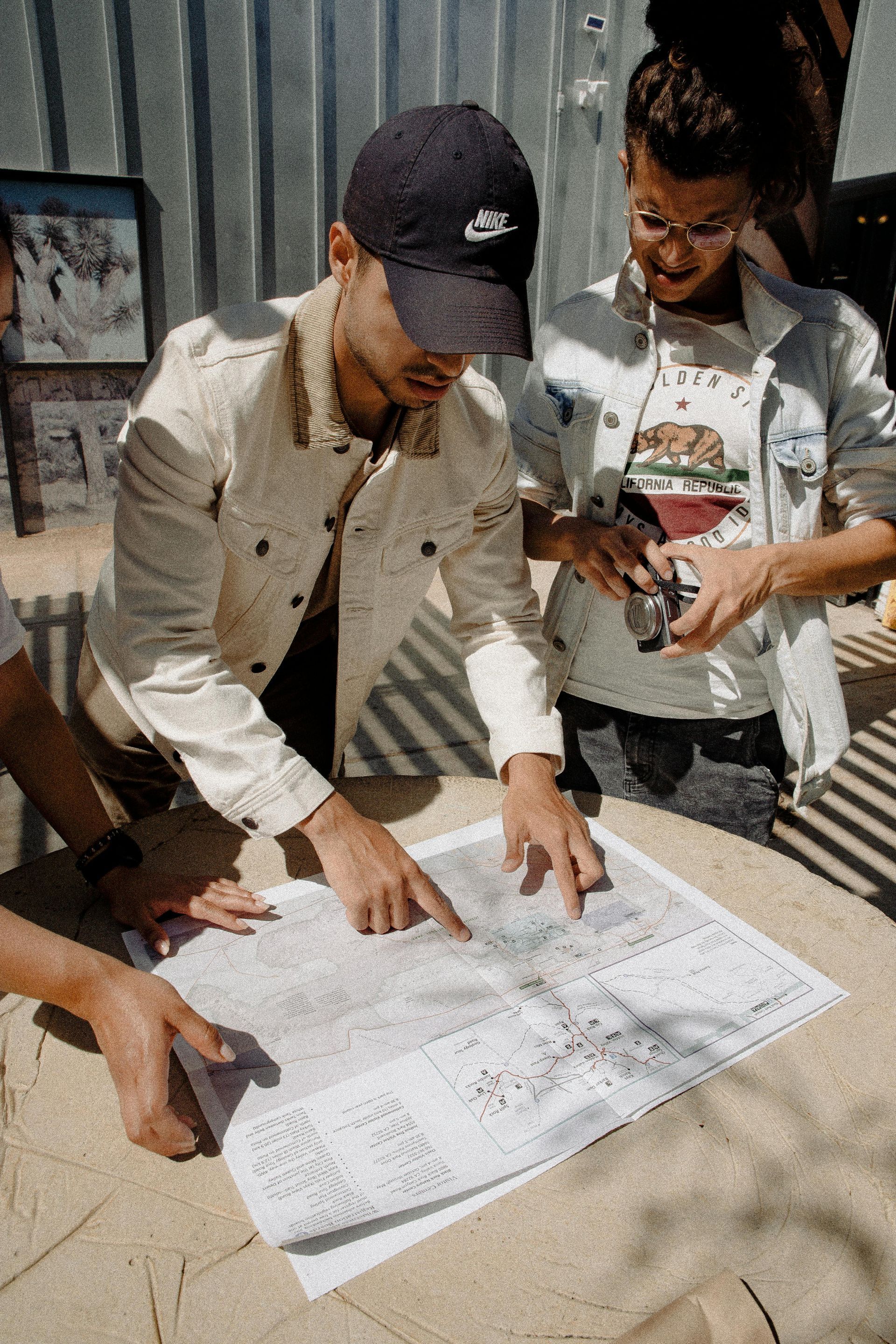 Two people, in casual wear, pointing at a map outdoors. One wears a Nike cap and jacket.