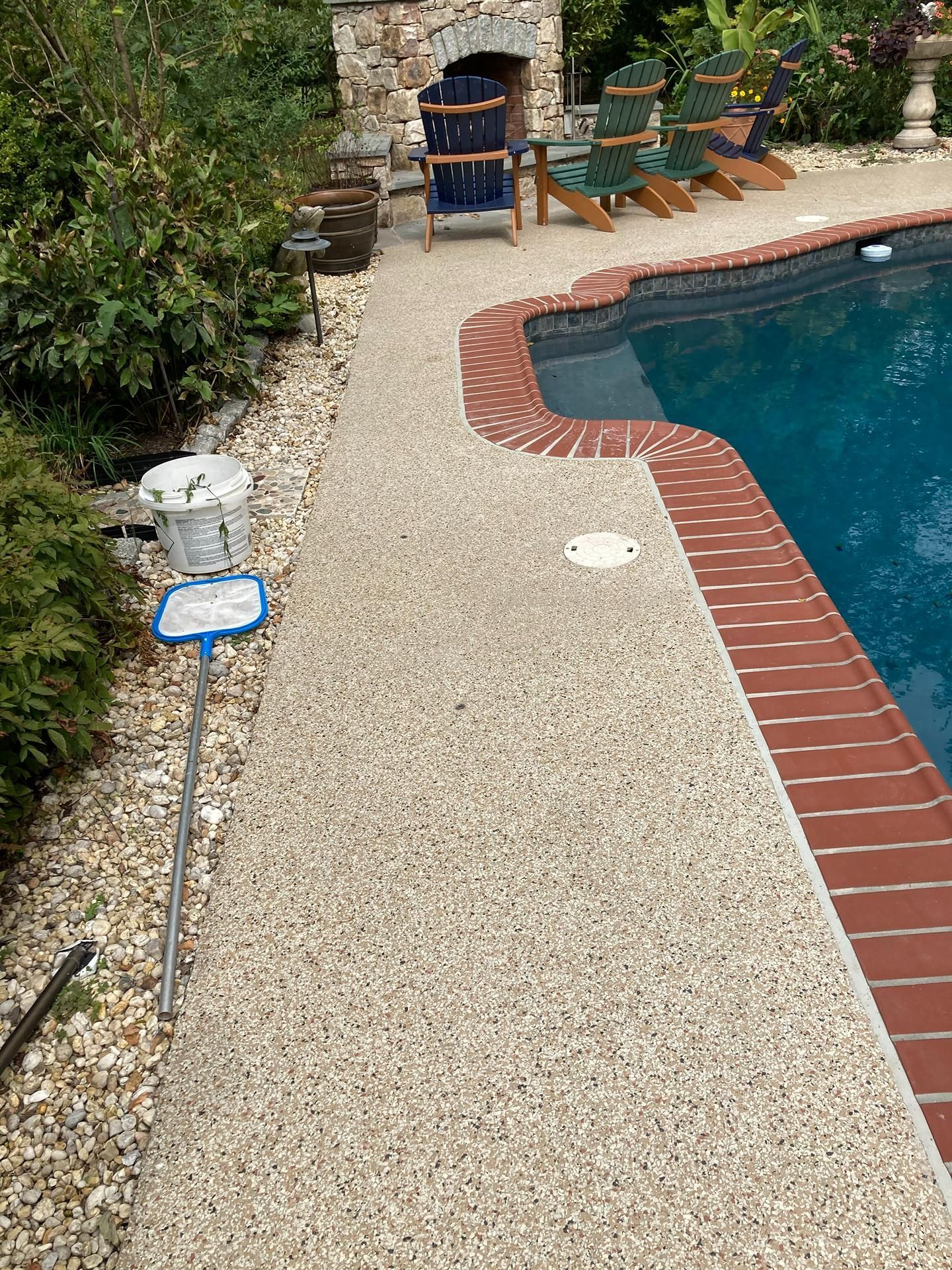 Gravel poolside path beside a blue pool, with lounge chairs and a brick grill area in the background
