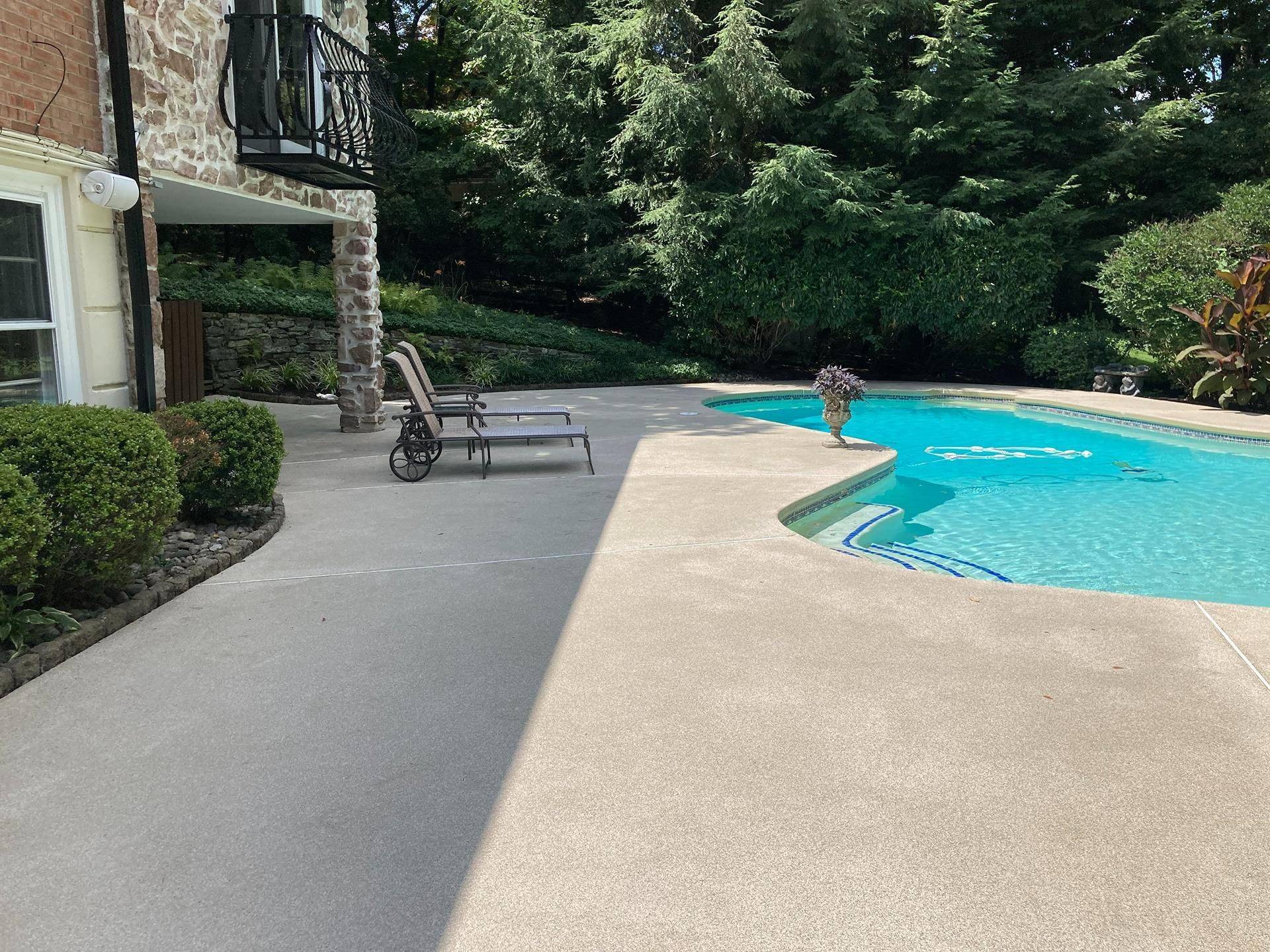 Outdoor pool with blue water, lounge chairs, and a patio beside a landscaped garden