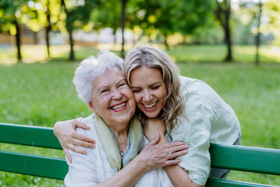 A young woman is hugging an older woman on a park bench.