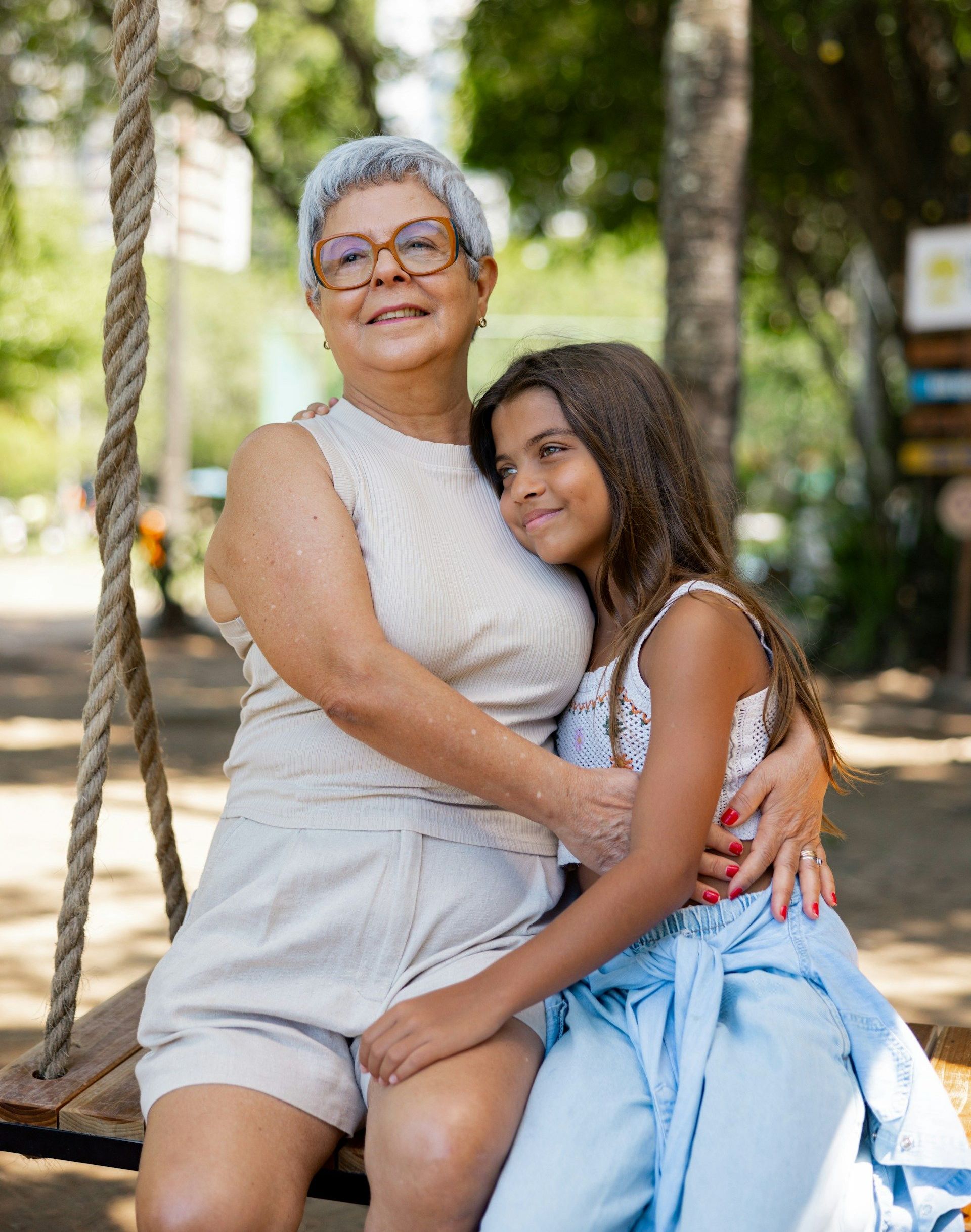 An elderly woman and a young girl are sitting on a swing.