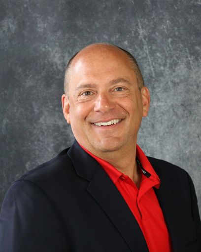 A man in a suit and red shirt is smiling for the camera.