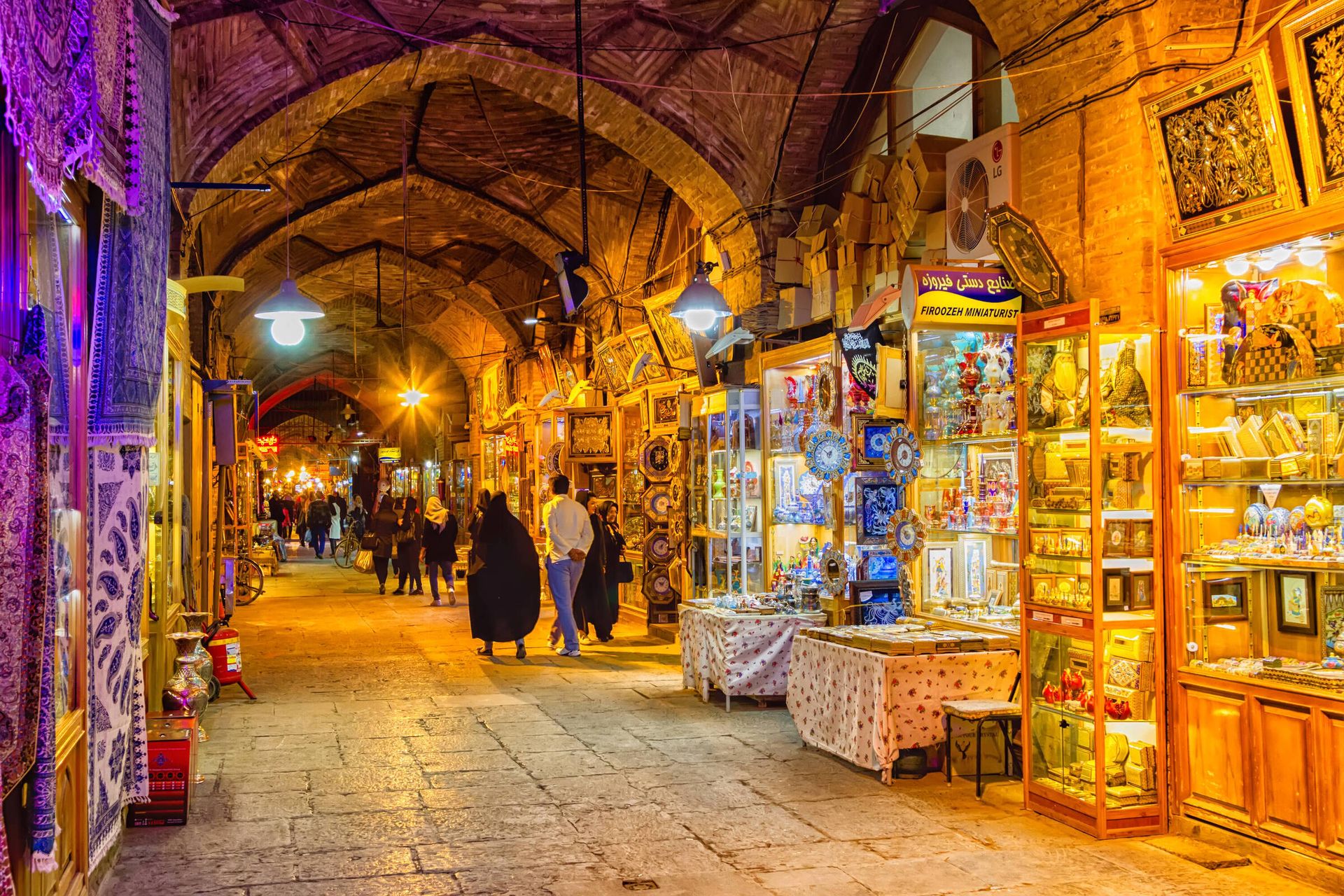 A group of people are walking down a narrow alleyway in a market at night.