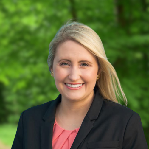 A woman in a red dress is standing in front of a brick building.
