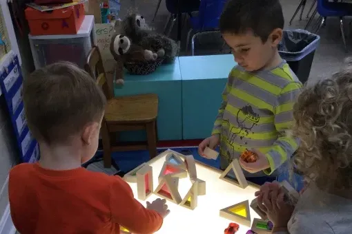 A group of children are playing with blocks on a light table.