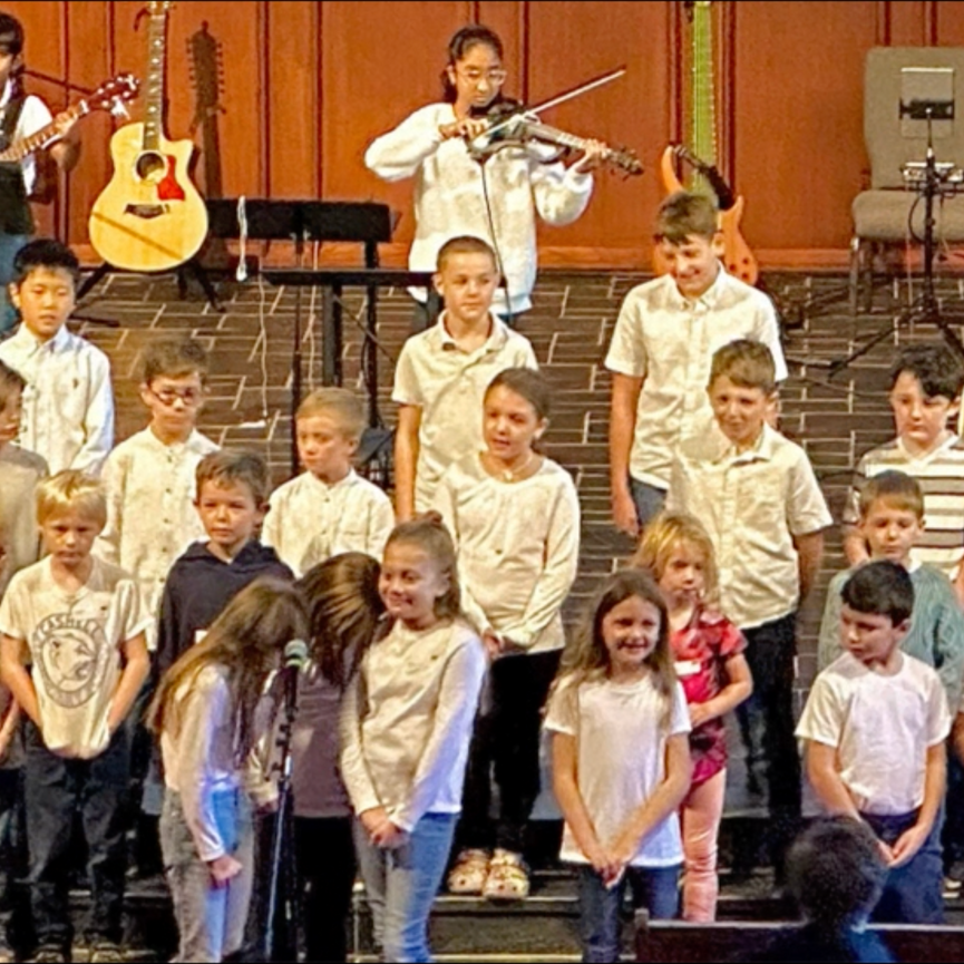 Group of children performing music on stage. Some play instruments. Others sing.