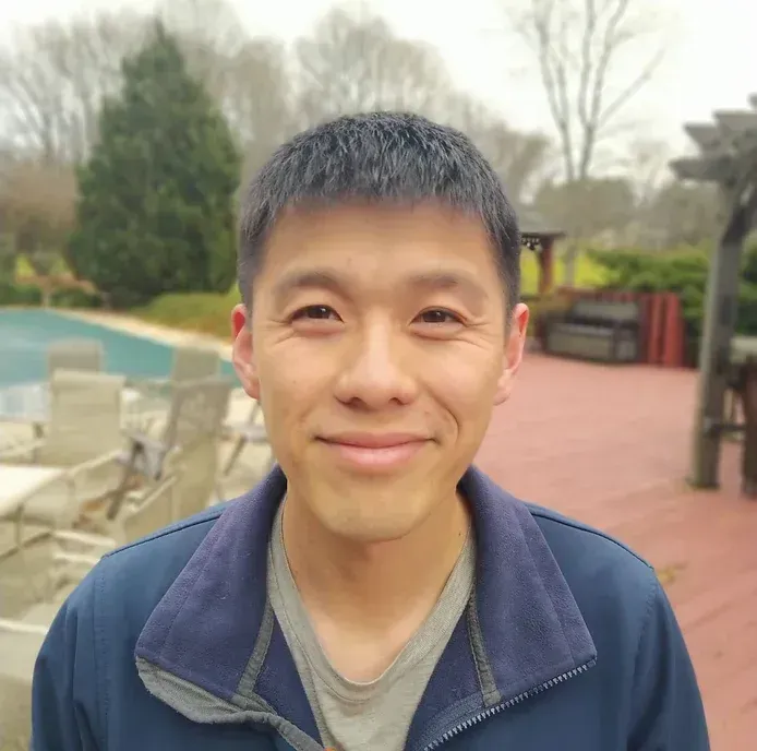A man in a blue jacket is smiling in front of a pool