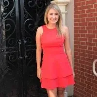 A woman in a red dress is standing in front of a brick building.