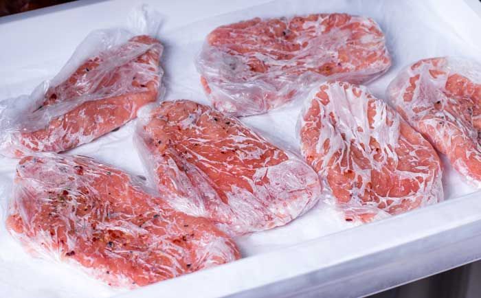 Una bandeja blanca llena de carne congelada envuelta en plástico.