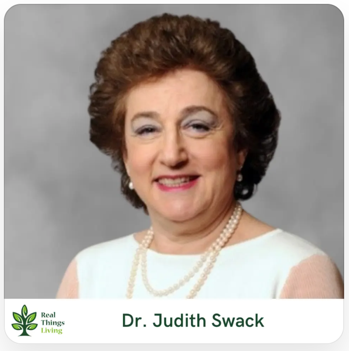 Portrait of Dr. Judith Swack smiling in a white top and pearl necklace against a gray background