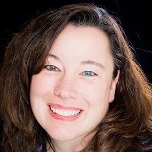 Woman with brown and blue eyes smiles at the camera, dark hair against a black background.