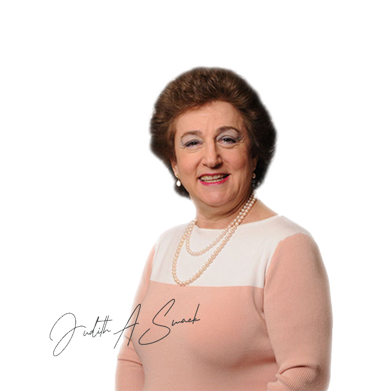 Woman wearing pearls and a pink sweater smiles. Her signature is visible.