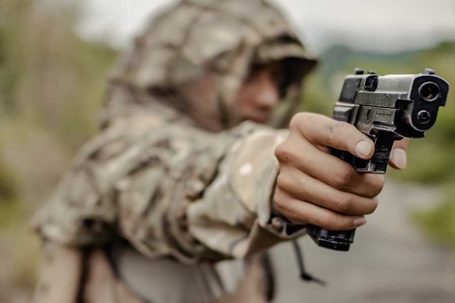 Person in camouflage aiming a handgun outdoors.