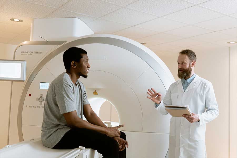 Man in MRI machine room consults with a doctor holding a tablet.