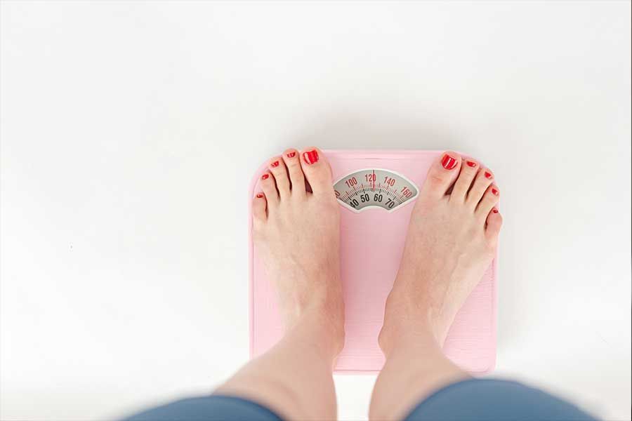 Feet on a pink scale, red toenails, white background.