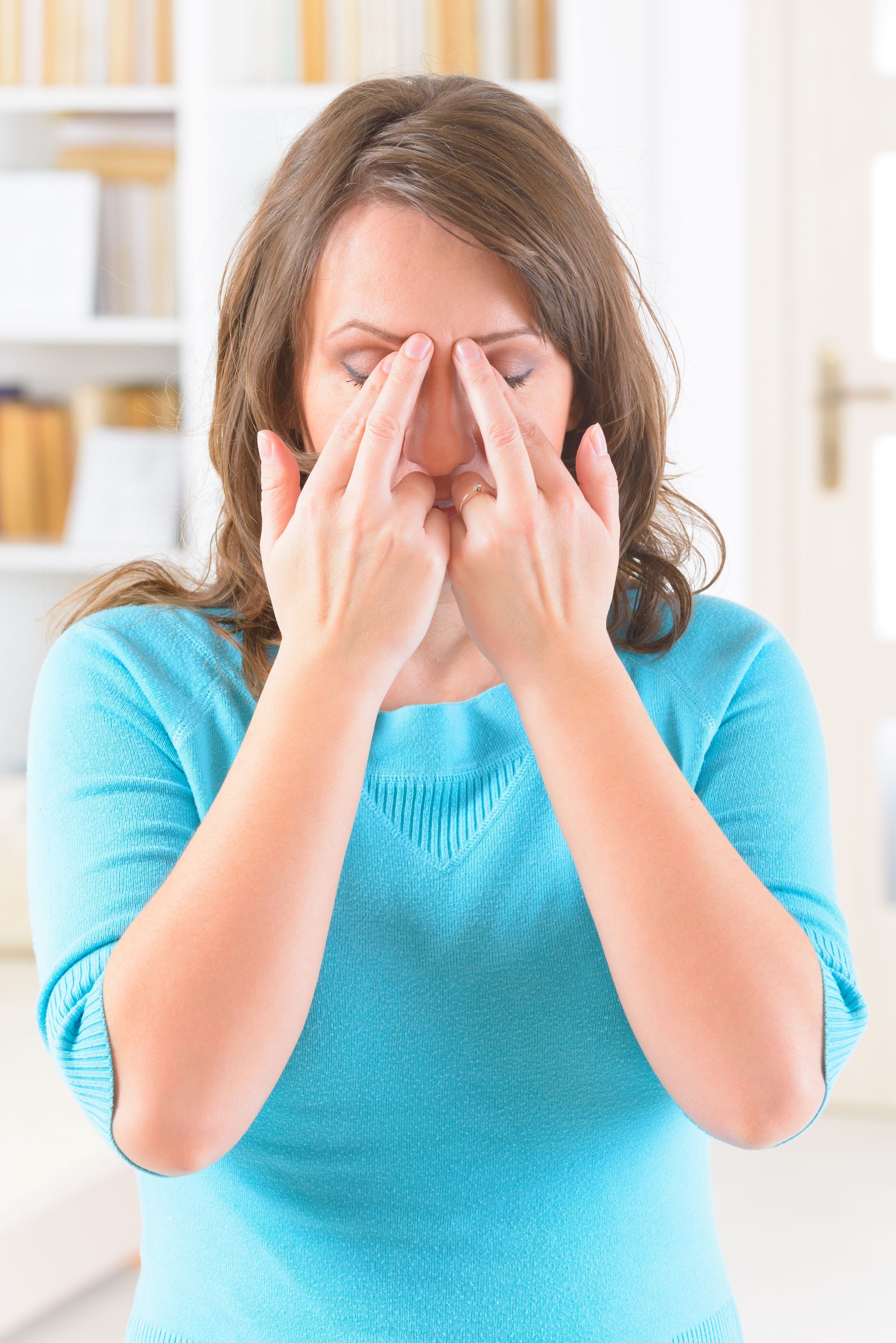 Woman with eyes closed, fingers on bridge of nose, wearing a blue shirt.