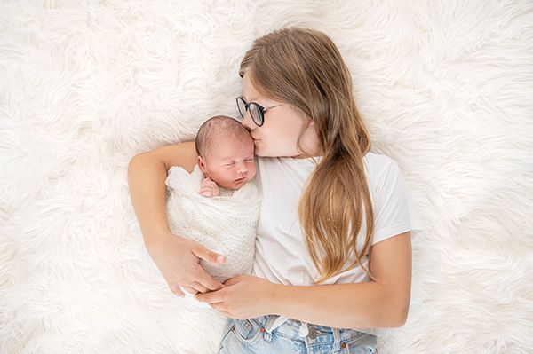 Große Schwester hält neugeborenes Baby beim Newborn Shooting in München