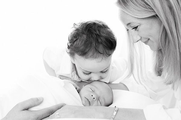 Liebevolles Babyfoto mit Mutter und Bruder – professionelle Neugeborenenfotografie zu Hause