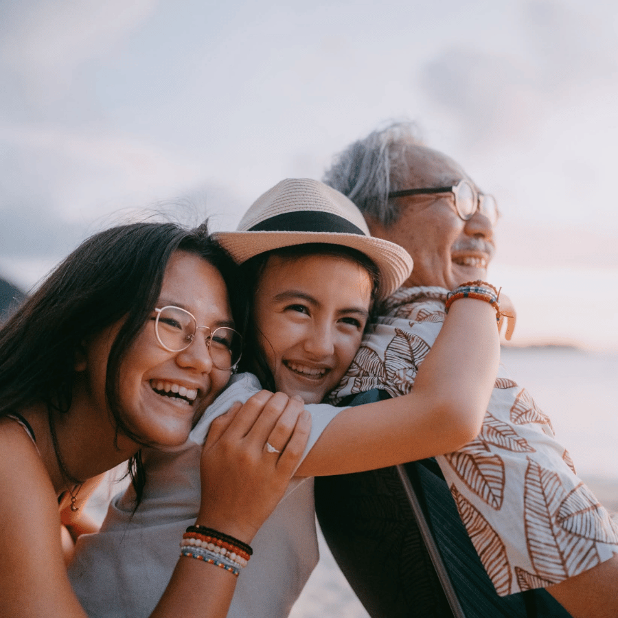 Three friends smiling and hugging outdoors at sunset, wearing casual clothes and hats
