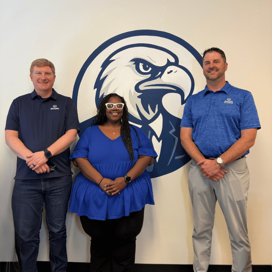 Three employees standing in front of a large eagle logo on a wall.