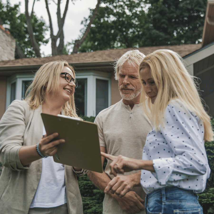 Three people reviewing a tablet outdoors in front of a house
