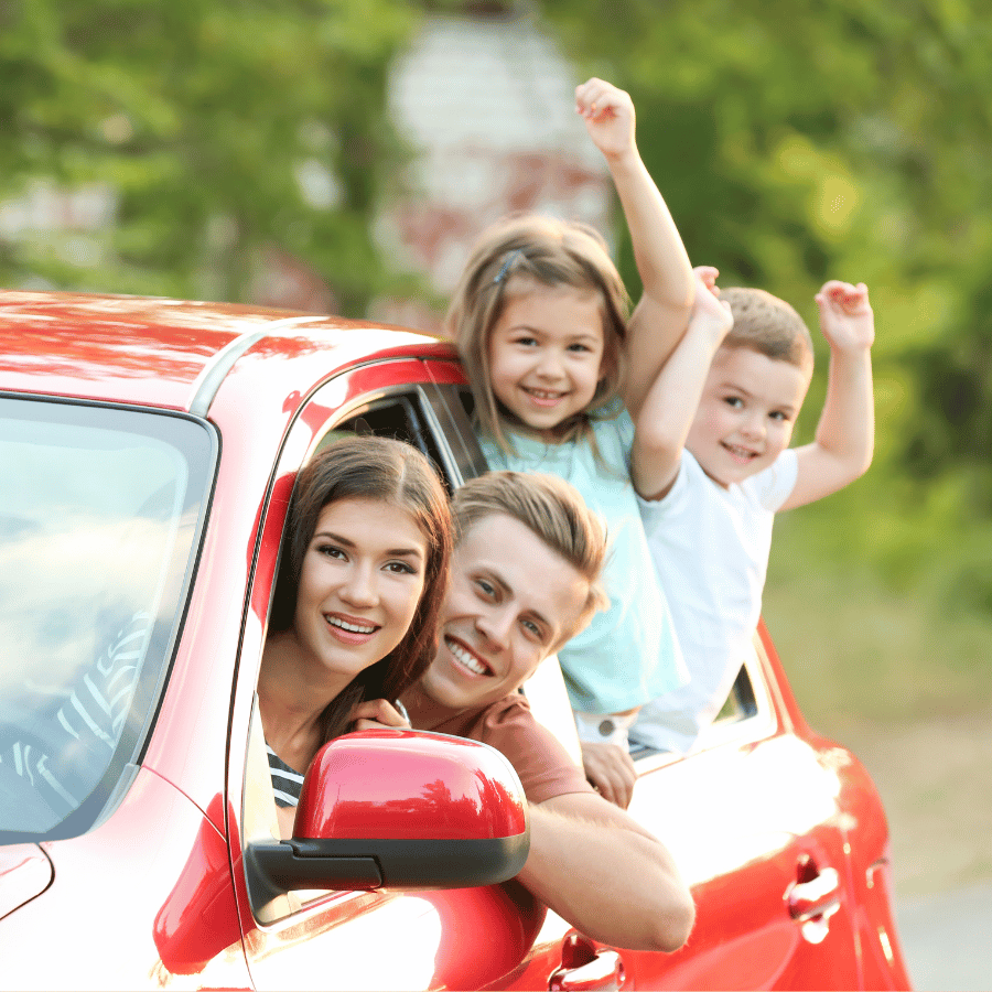 Family waving from a red car on a sunny day