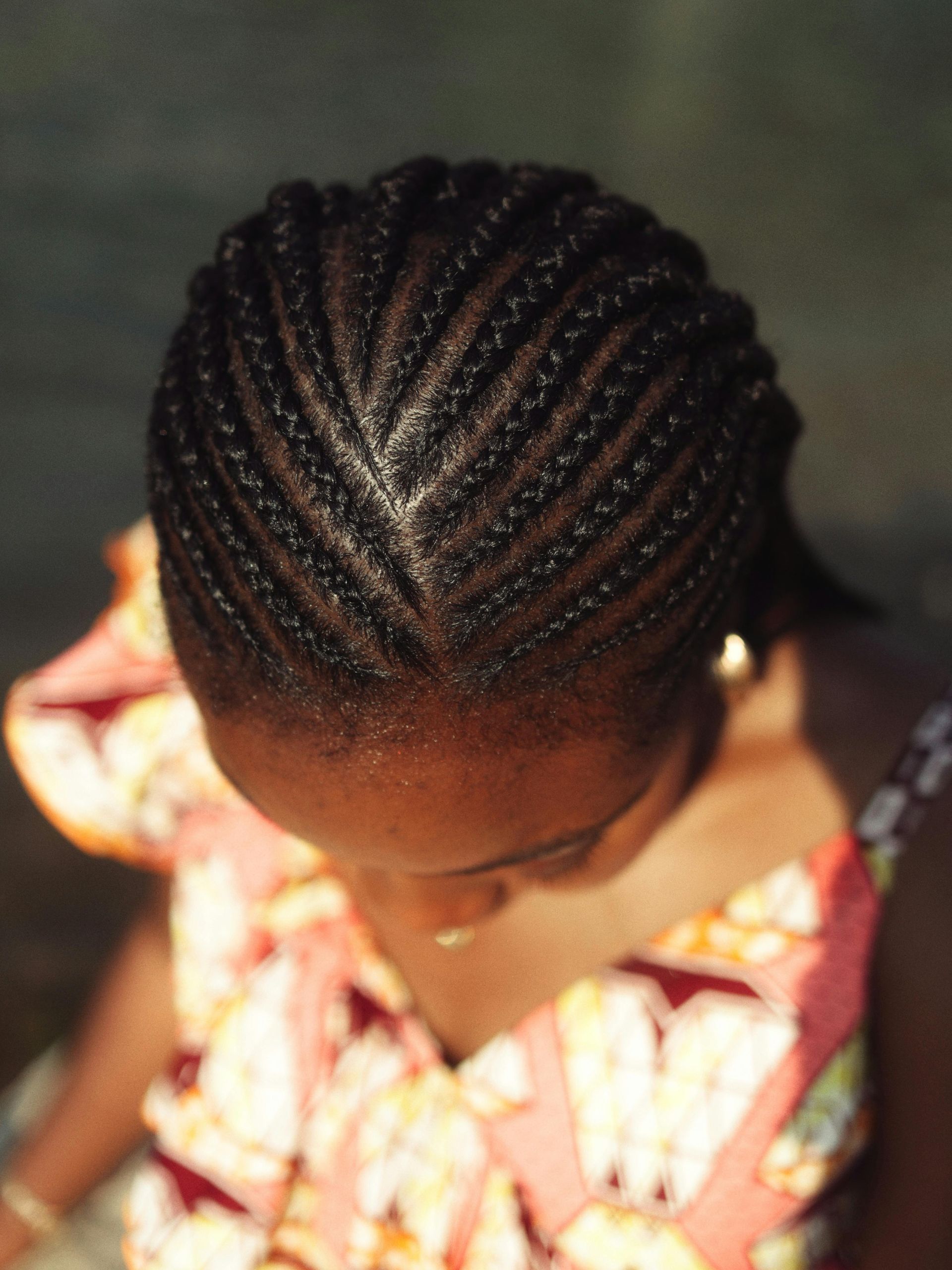 Close-up of a person's head, showing braided hair in a geometric pattern.