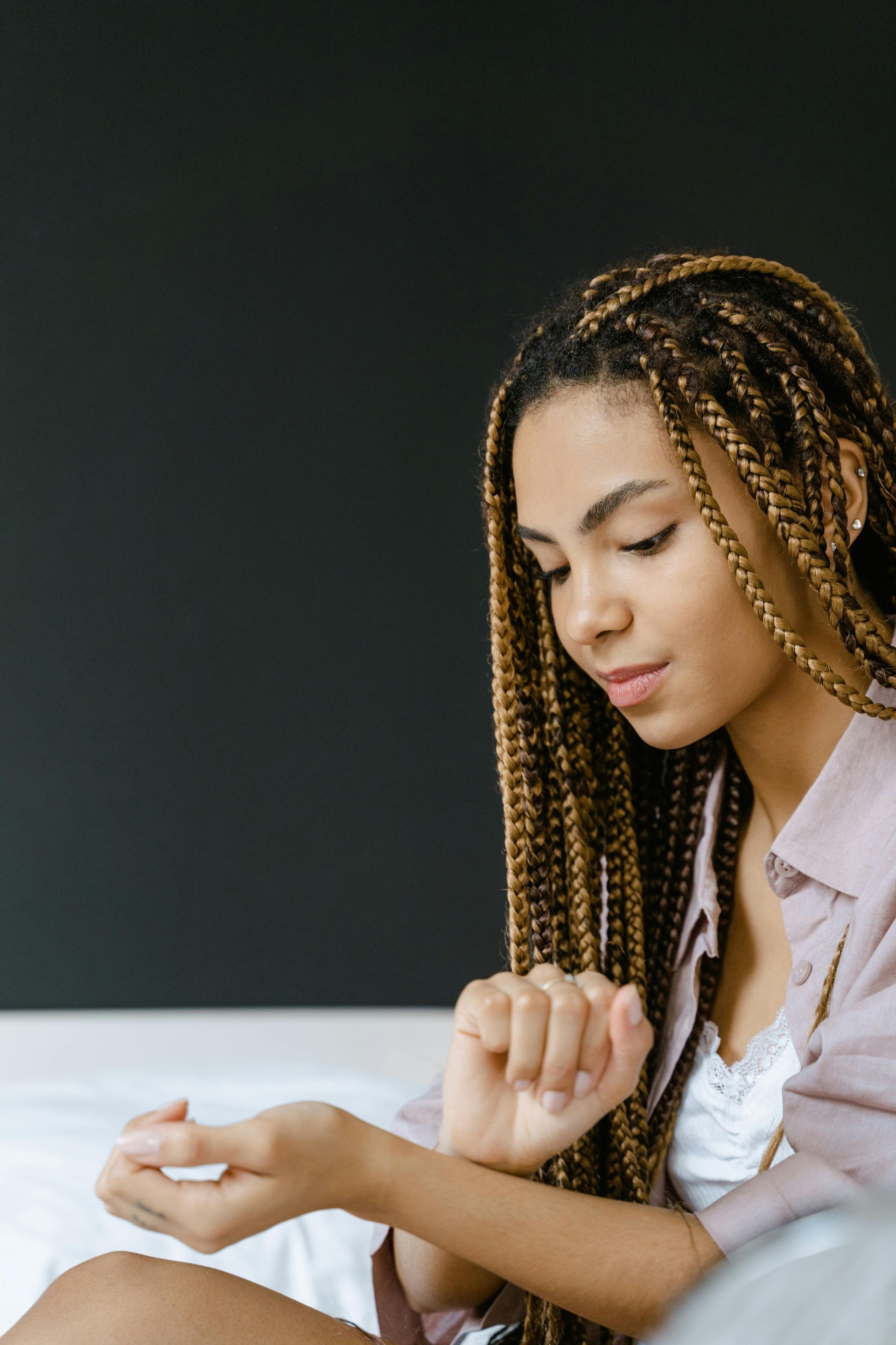 Woman with long braids looking at her wrist in a room with a black wall.