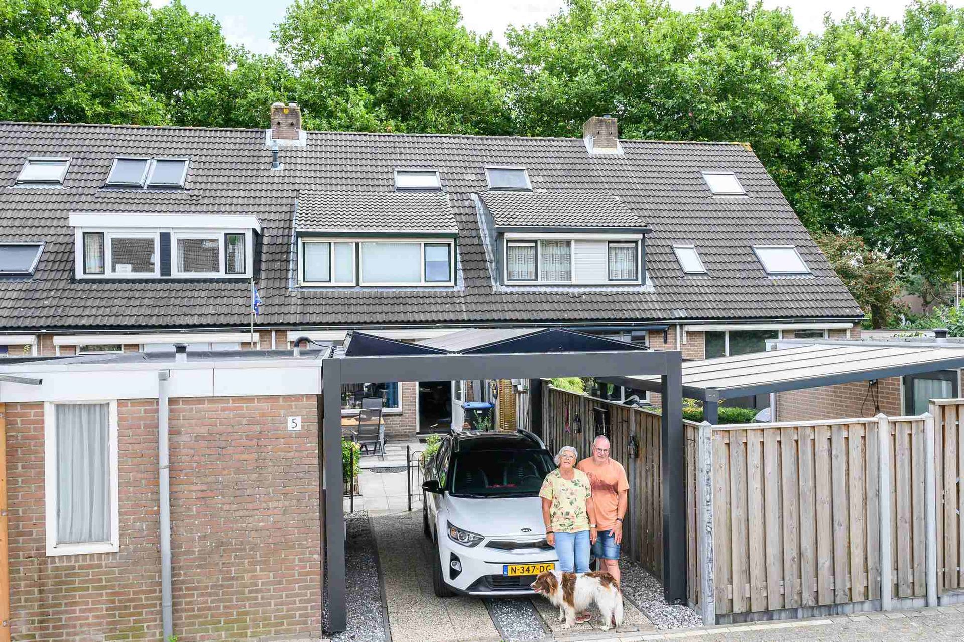 Een stel en een hond staan voor een auto op de oprit.