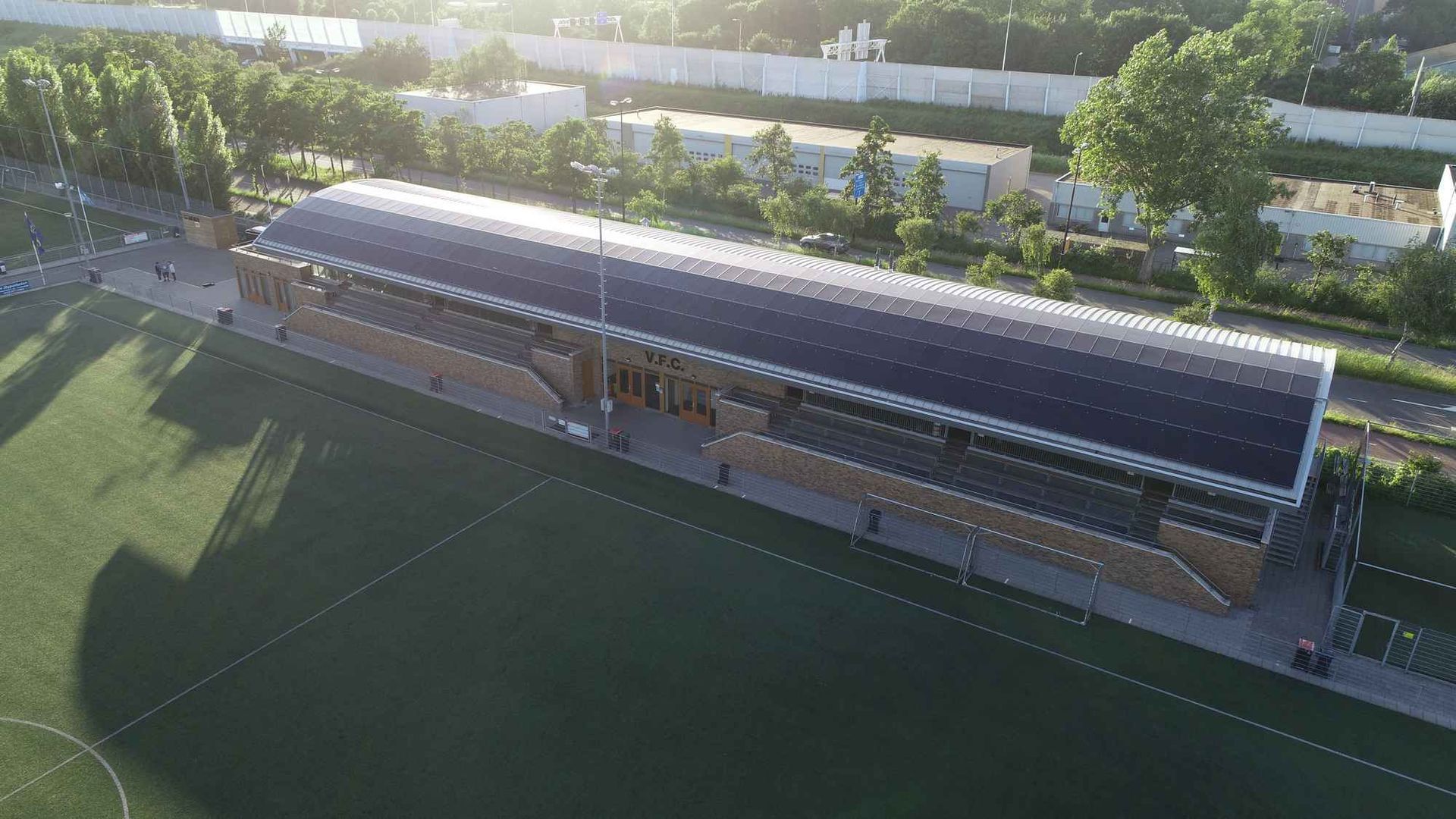 Een luchtfoto van een voetbalveld met een groot stadion op de achtergrond.