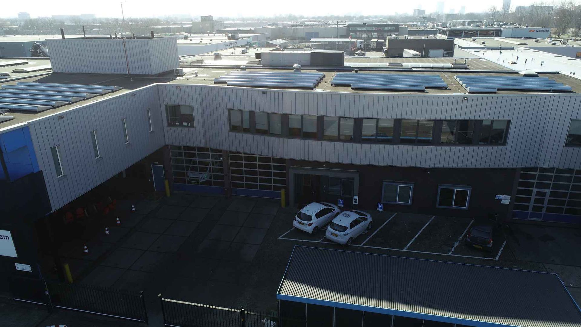 Een luchtfoto van een groot gebouw met daarvoor geparkeerde auto's.