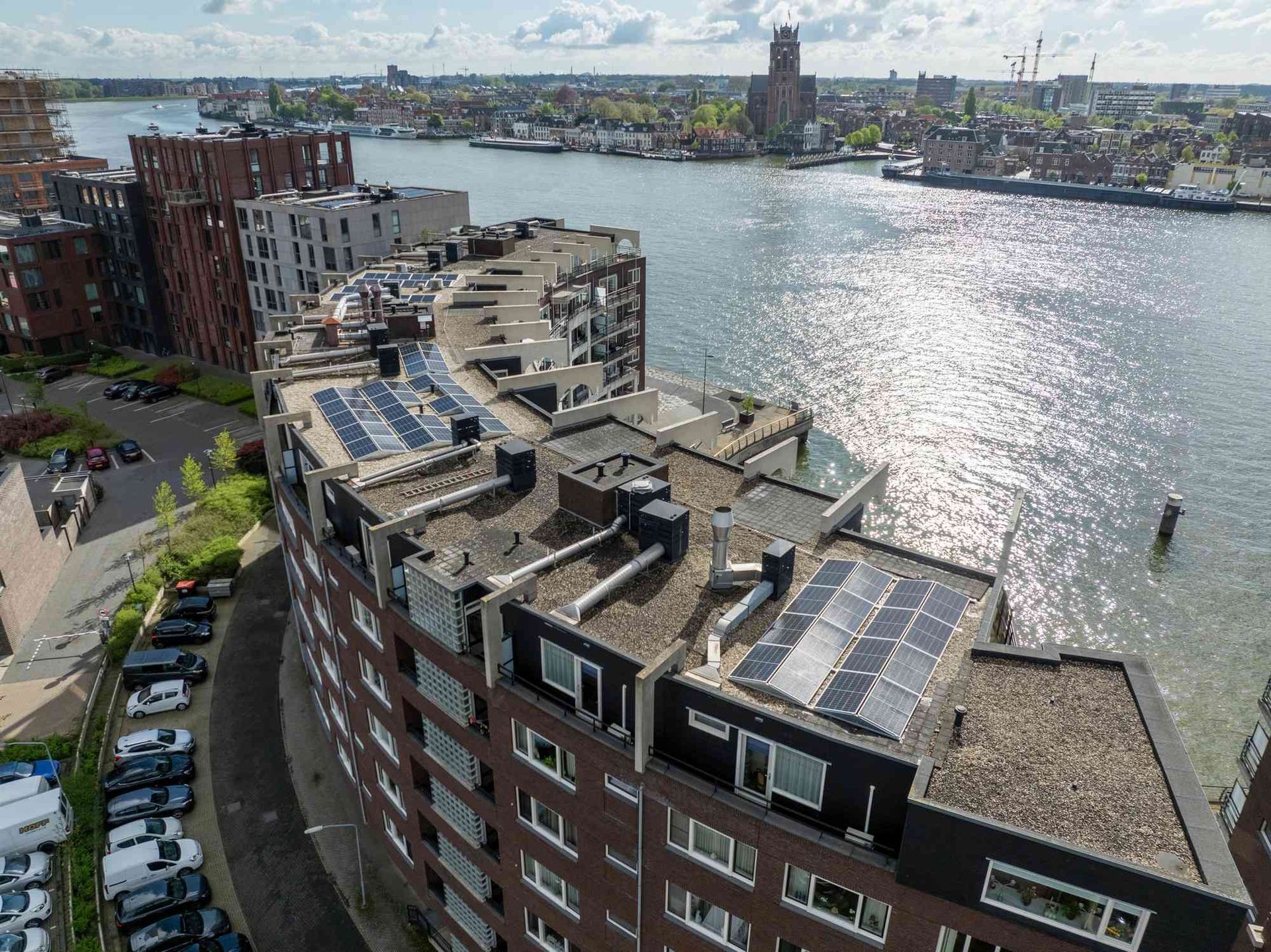 Een luchtfoto van een gebouw met zonnepanelen op het dak, met uitzicht op een waterlichaam.