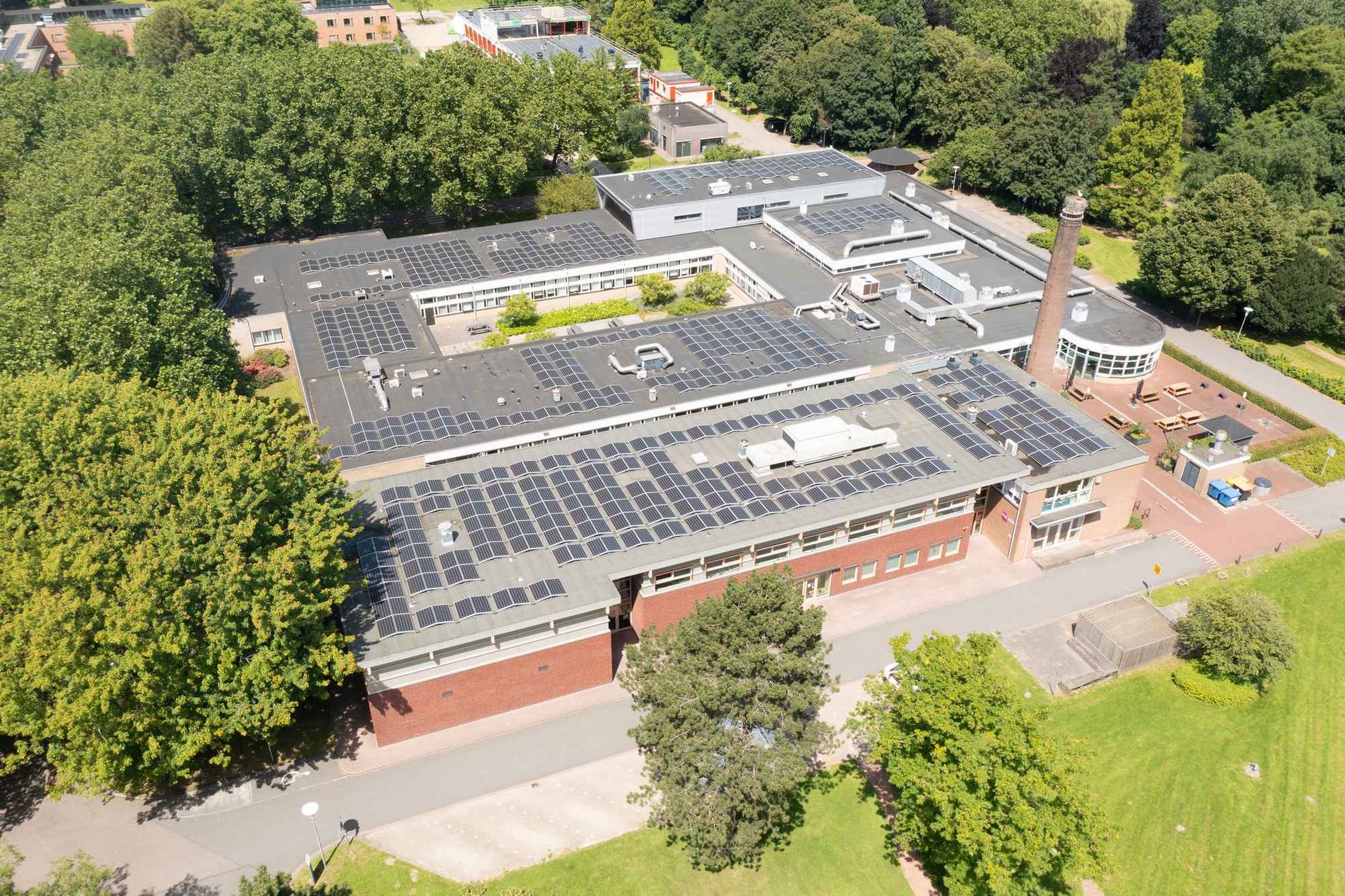 Een luchtfoto van een groot gebouw met zonnepanelen op het dak, omgeven door bomen.