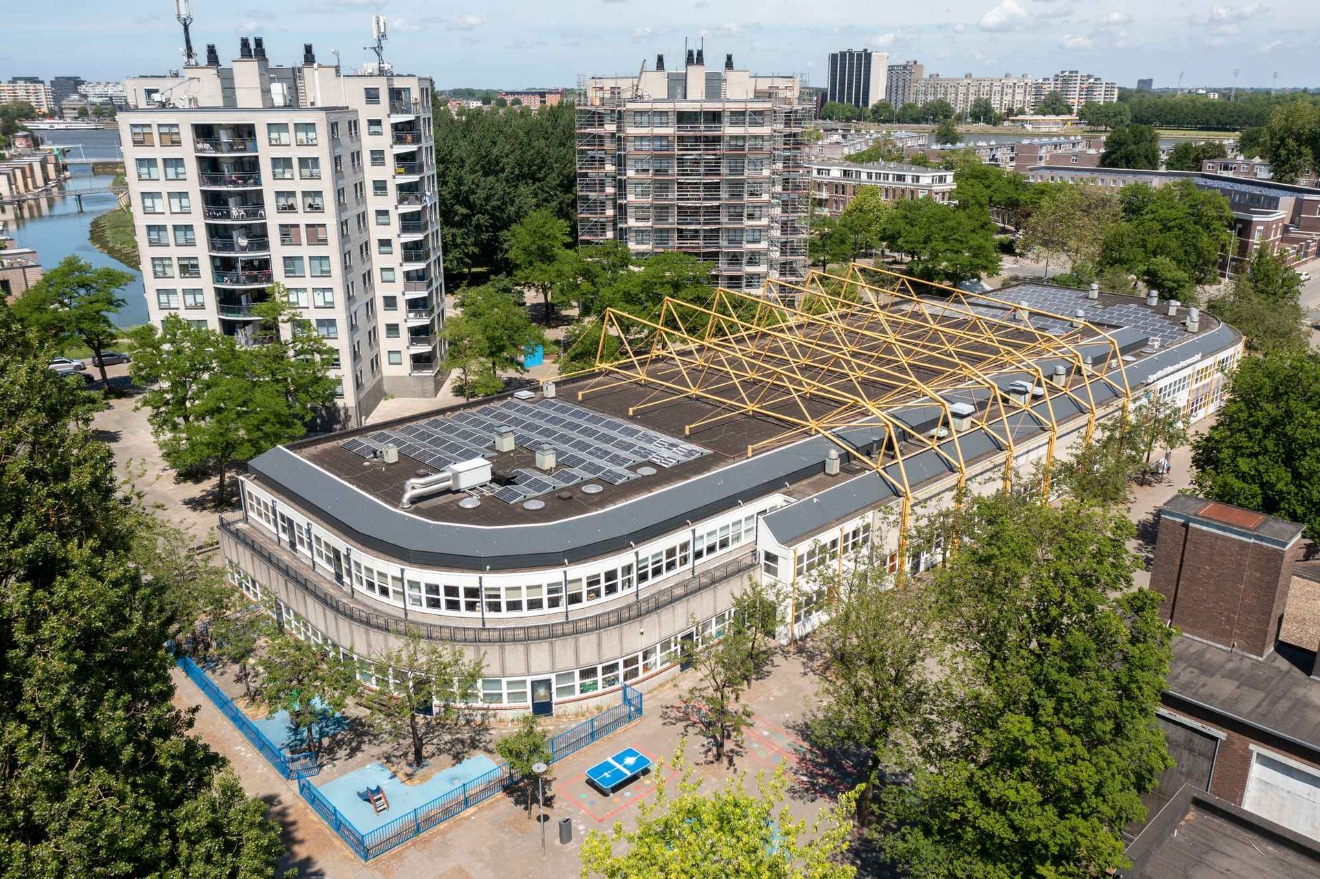 Een luchtfoto van een groot gebouw in een stad, omgeven door bomen.
