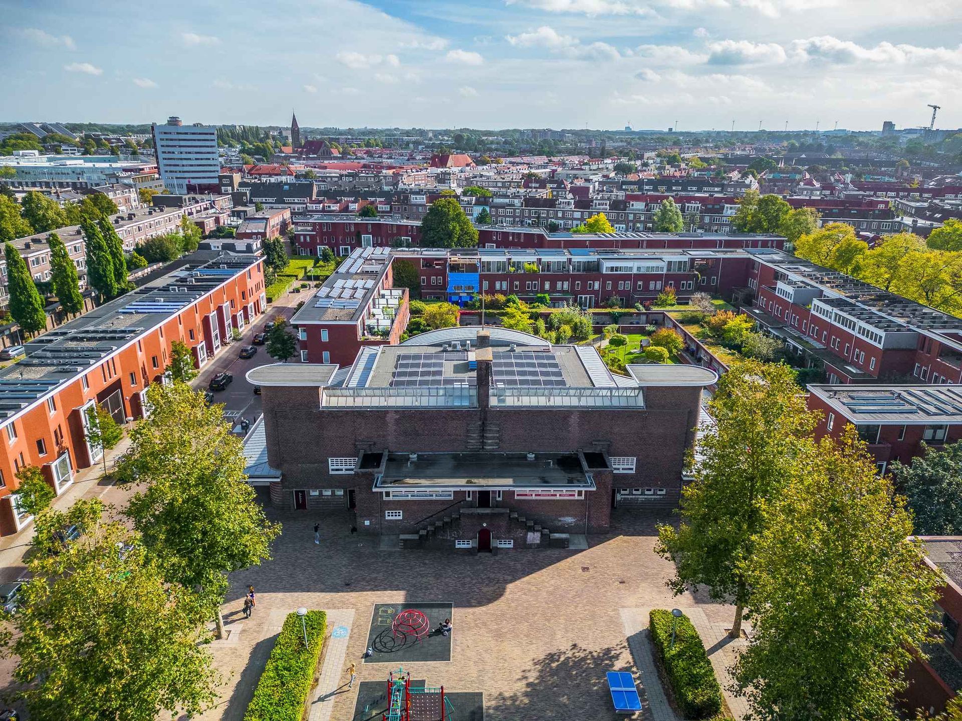 Een luchtfoto van een groot gebouw midden in een stad, omgeven door bomen.